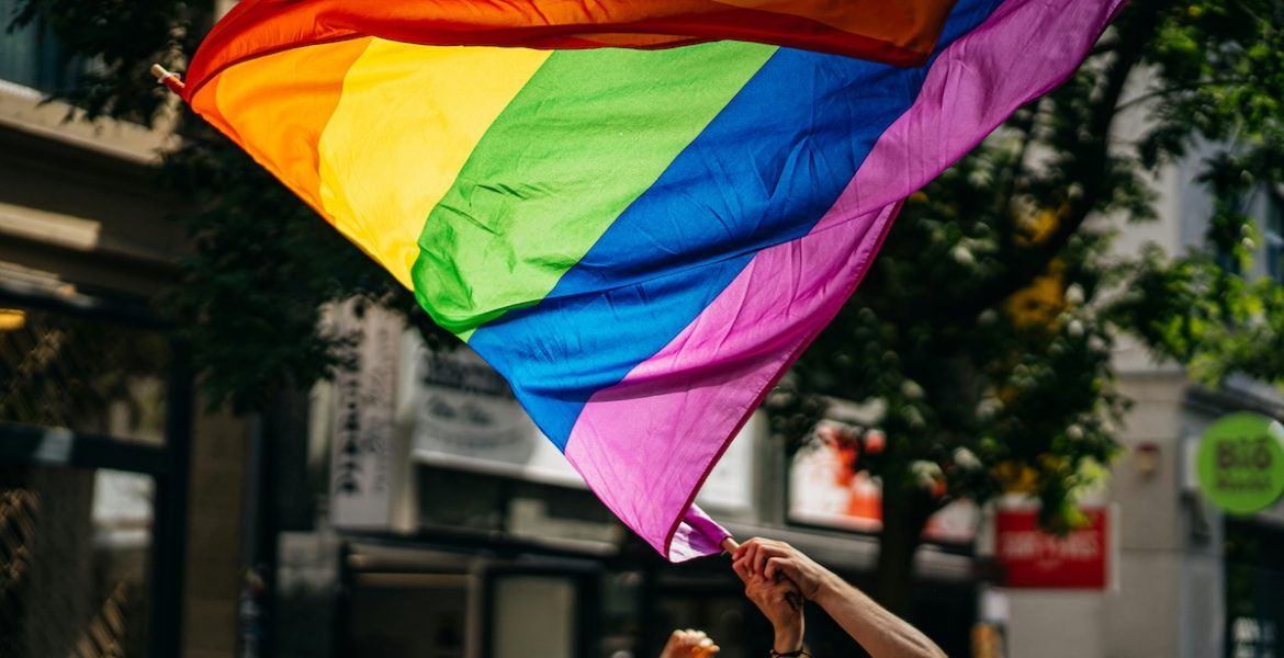 Crowd holding rainbow Pride flags during a daytime march.